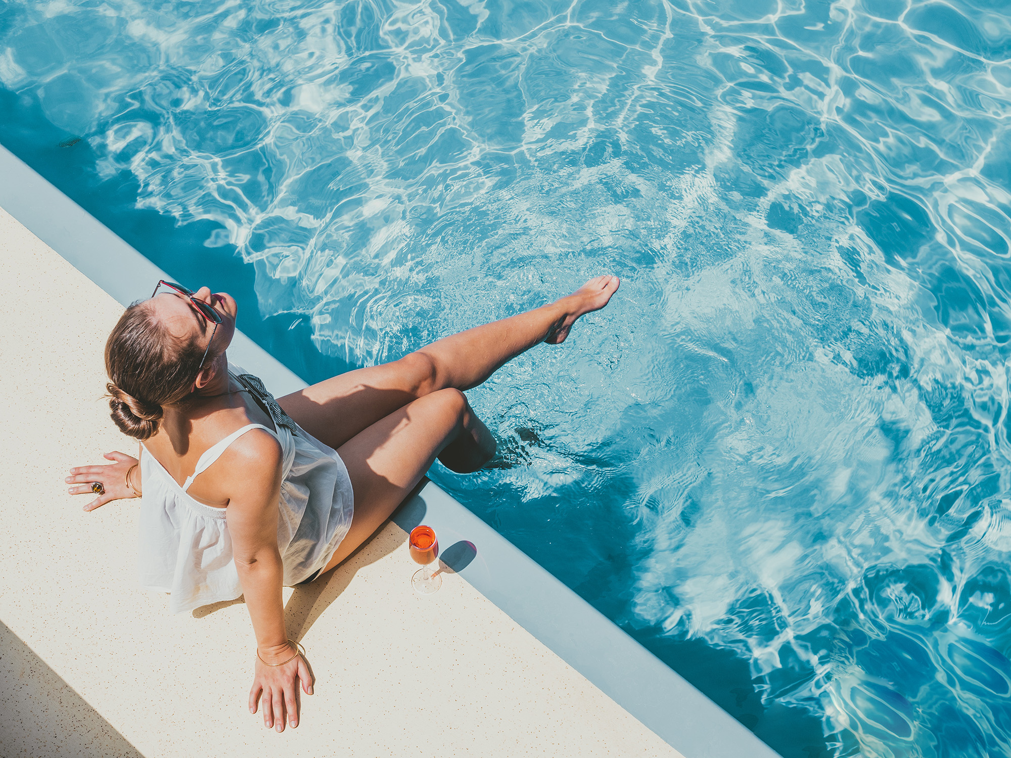 woman sitting by edge of swimming pool splashing