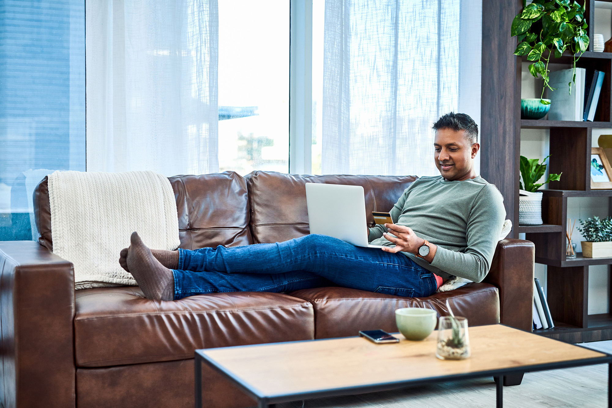 man on couch doing online shopping with laptop computer